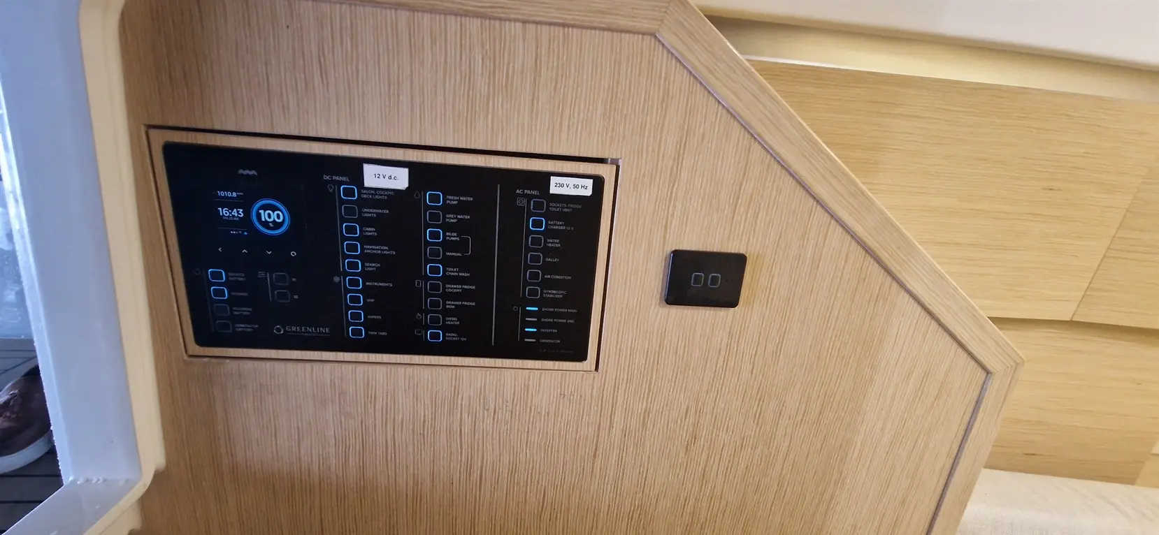 Control panel displaying battery, AC, and DC functions with numerical data, set within a wooden interior setting.